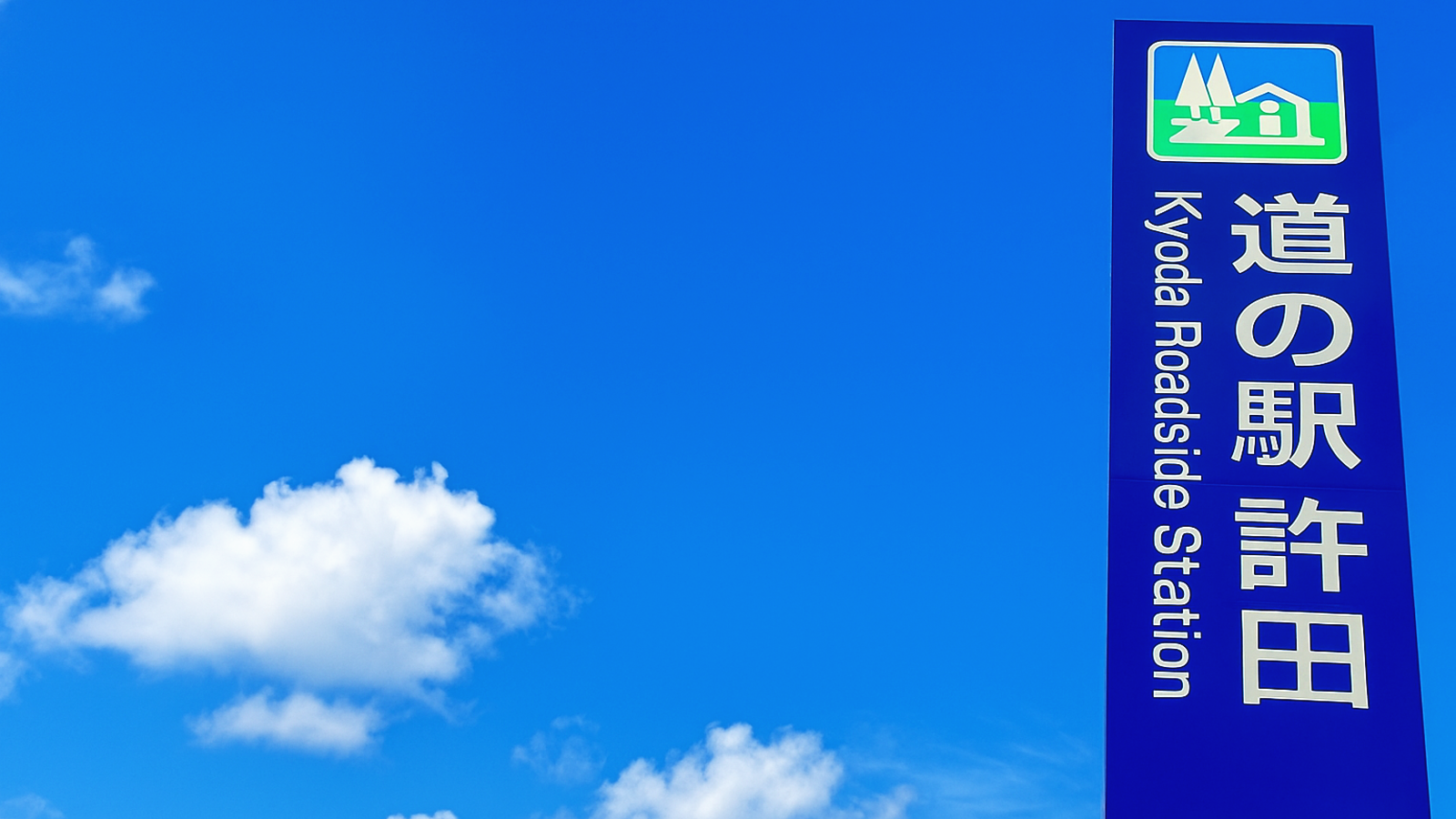 澄んだ青空の下に立つ「道の駅許田」の縦型看板と、背景に広がる白い雲。